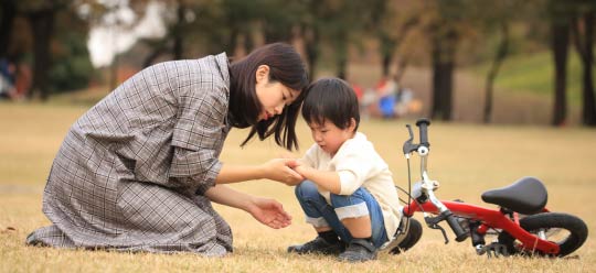 遊具がある公園で、足を抱えて泣いている子どもと、心配そうに駆け寄る母親